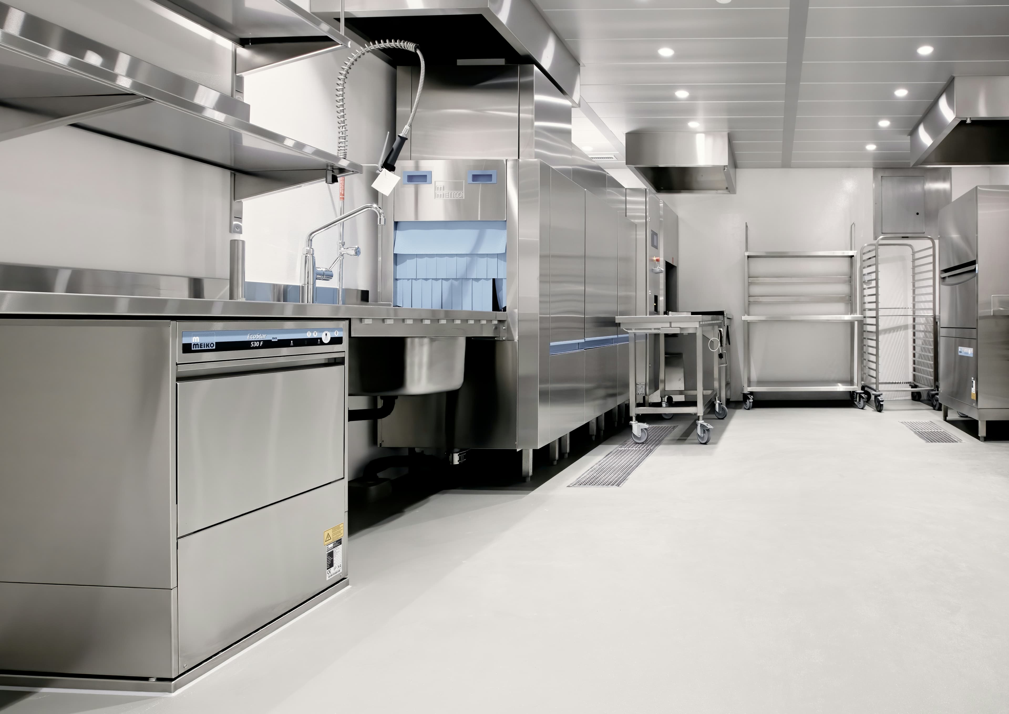A pristine stainless-steel commissary kitchen with sheet pan racks, prep tables, and exhaust hoods