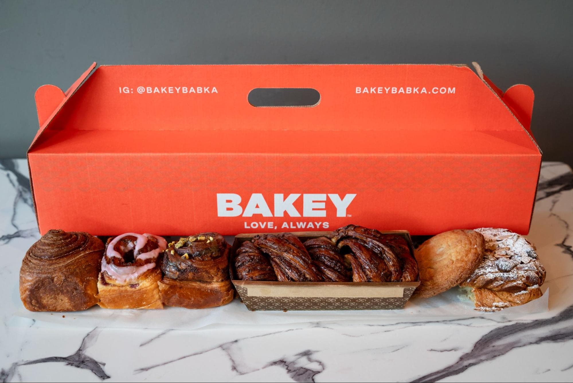 A signature Bakey box surrounded by laminated pastries on a marble counter