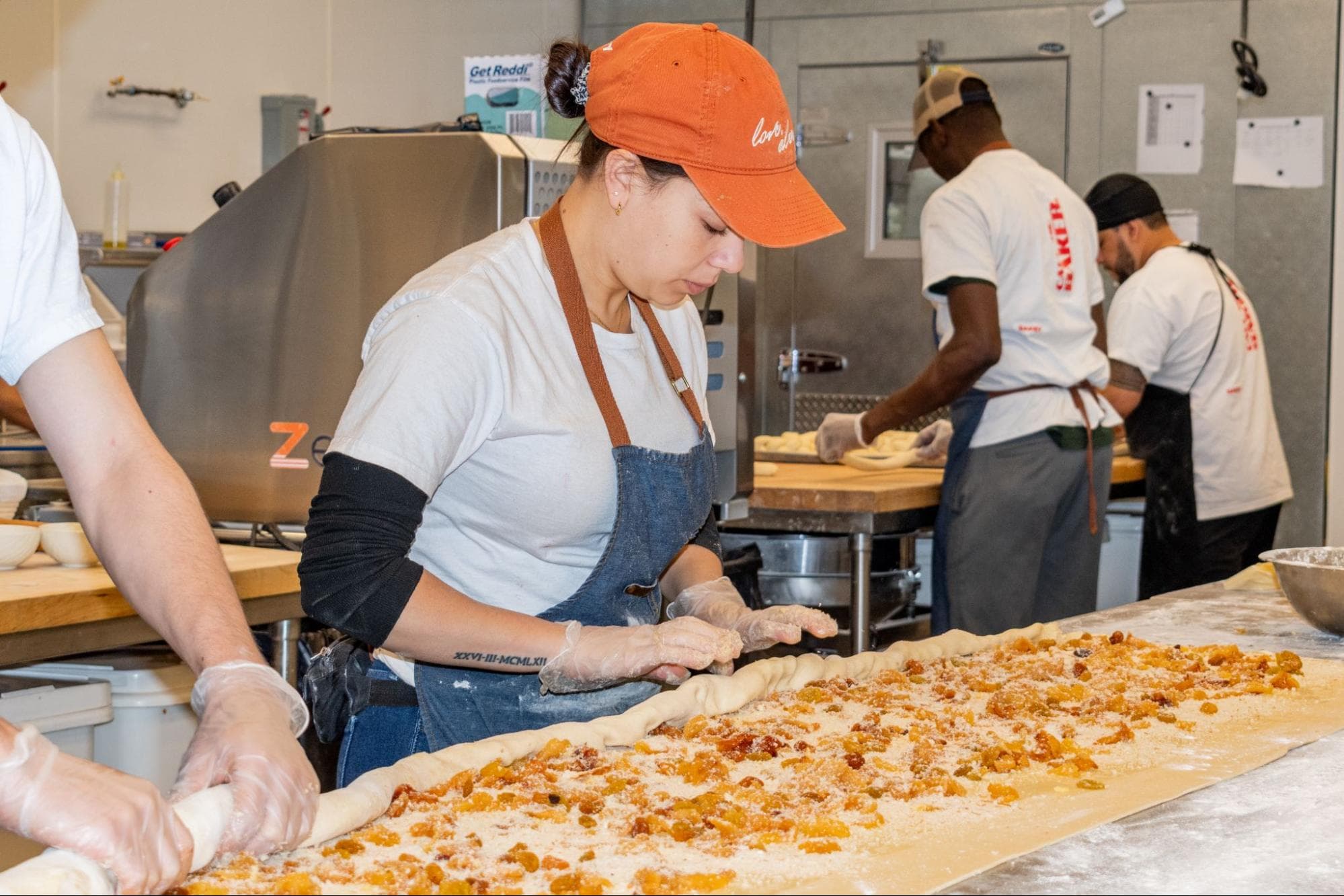 A baker shapes laminated dough on a long prep table inside the Bakey commissary