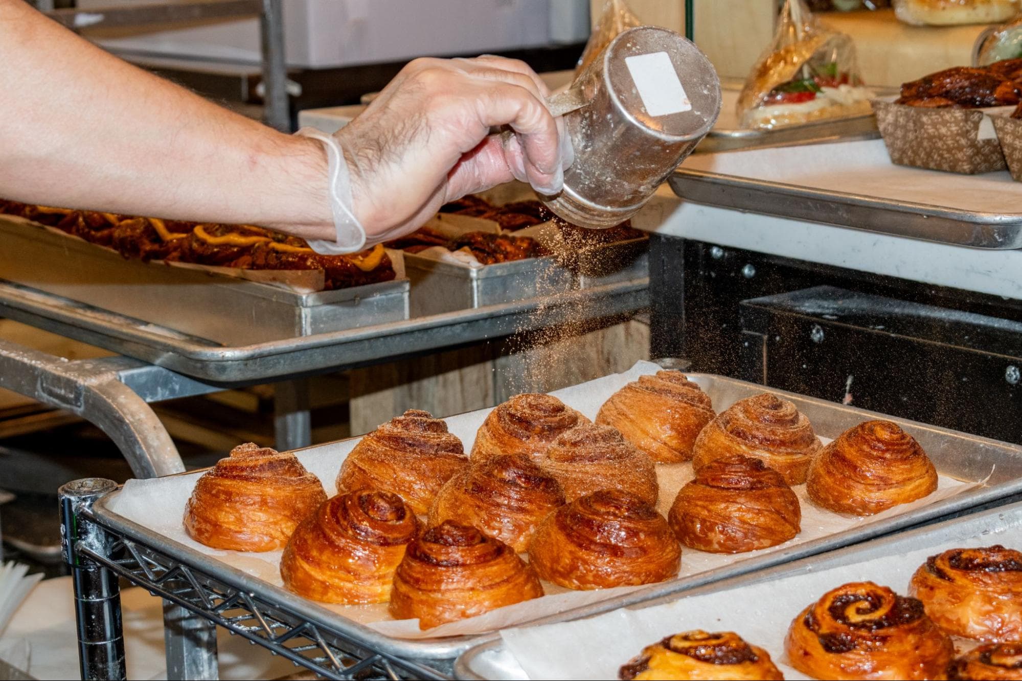 A baker dusts sugar over a tray of fresh-out-of-the-oven babkas