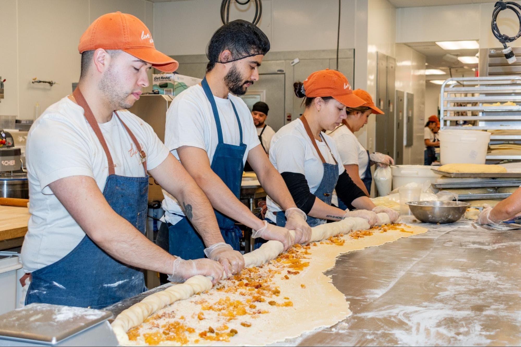 Bakey's bakers working side-by-side on a long stainless steel table, shaping laminated dough